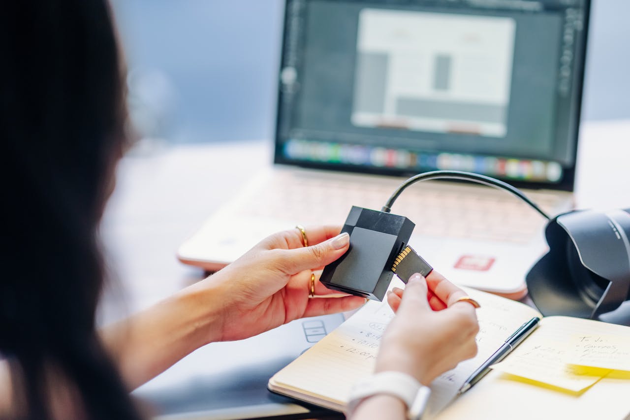 Close-up of hands using a memory card reader connected to a laptop, highlighting digital work essentials.